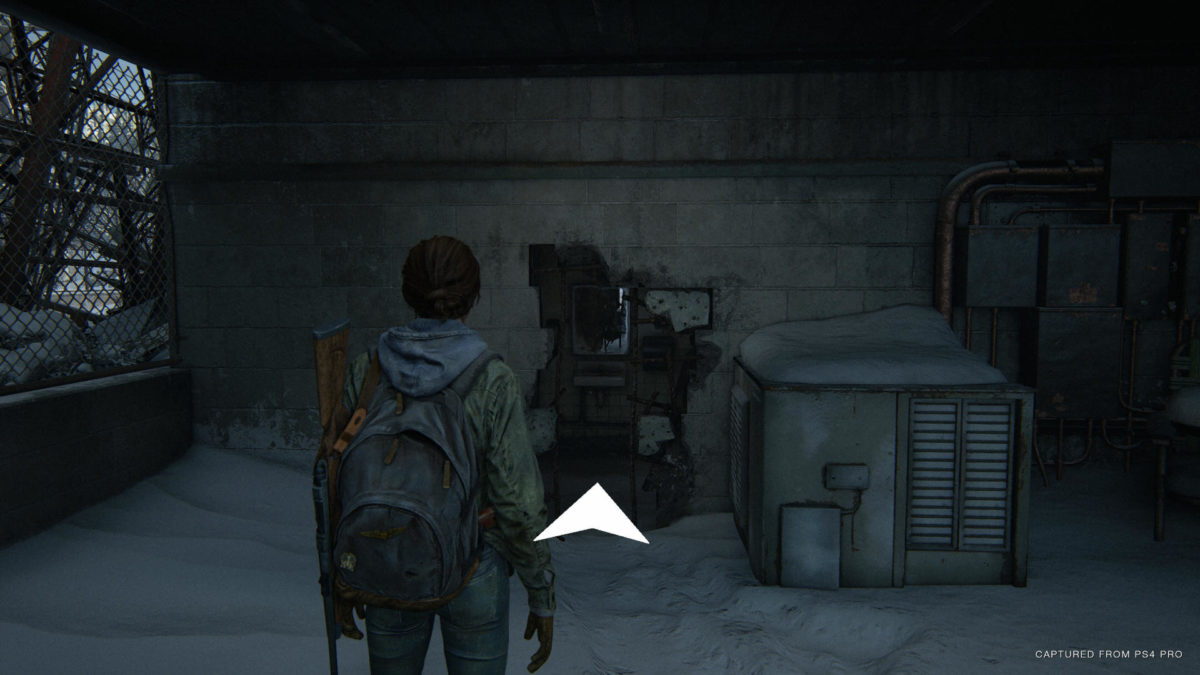 Ellie facing a wall that has a hole to pass through, and a big white arrow pointing in that direction as part of Navigation Assistance.