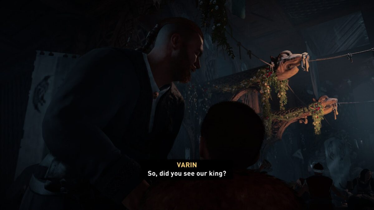 A man looking off to the right in a dimly lit room, which is decorated in party decor. Varin (in yellow): So, did you see our king?