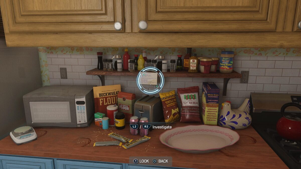 First person view of a kitchen counter and a shelf. On the bottom of the screen there are prompts to press L2 / R2, and there is a big circular reticle in the middle of the screen indicating that you found a clue.